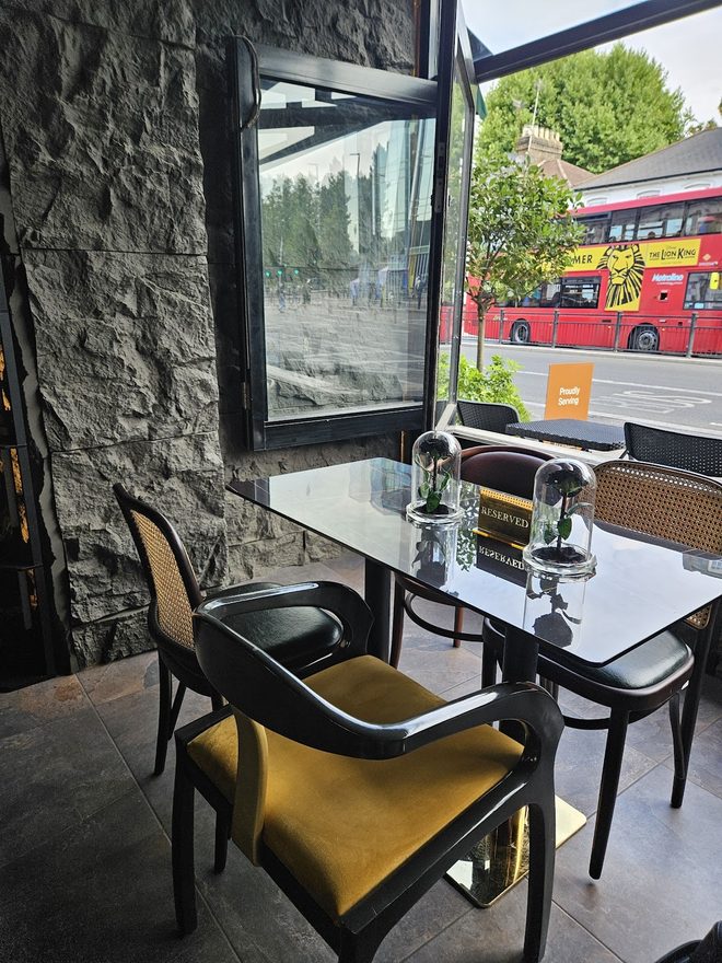 A marble table for two by the window with a red bus passing outside
