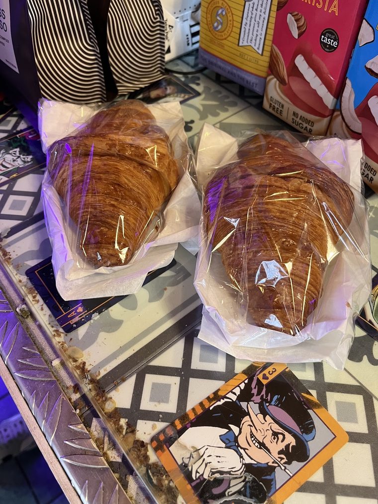 A glazed croissant-style pastry in a paper wrapper on the tiled counter