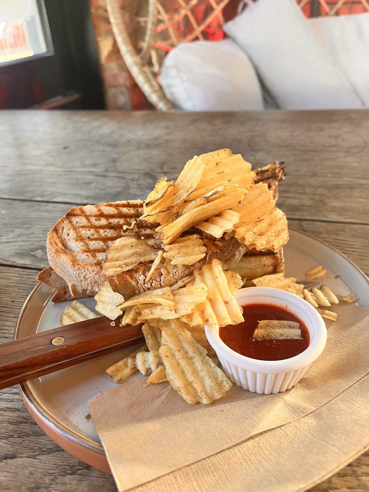 A toasted sandwich on a wooden board with crisps and dipping sauce